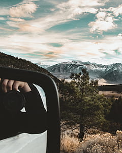 person taking photo of snow-covered mountain under cloudy blue sky thumbnail