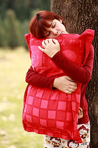 woman hugging red pillow beside tree during daytime thumbnail