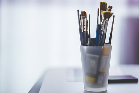 selective focus photo of assorted-color paintbrush in clear glass cup on gray surface thumbnail