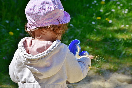 toddler girl holding blue plastic toy while throwing sand thumbnail