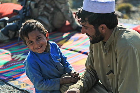 smiling boy in blue jacket beside man in green thobe during daytime thumbnail
