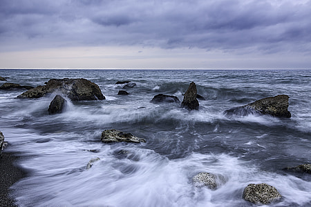 seashore with medium rocks and waves under white cloudy sky at daytime thumbnail