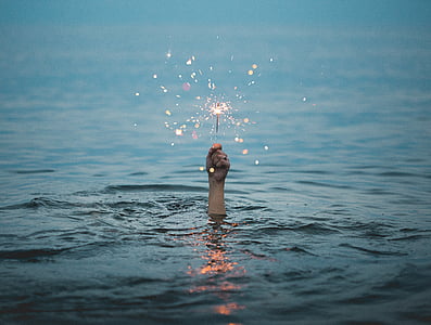 person holding sparkler in sea during daytime thumbnail
