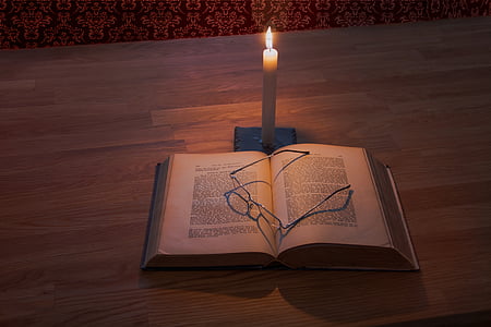 eyeglasses on top of open book beside lighted candle thumbnail
