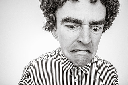 curly-haired man with and grumpy face wearing stripe collared shirt close-up and grayscale photo thumbnail