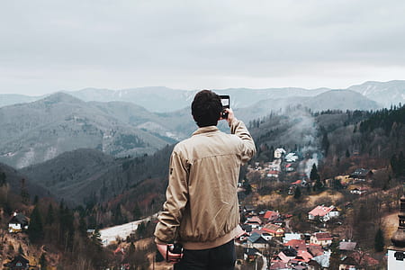 person in brown jacket took a photo of mountain thumbnail