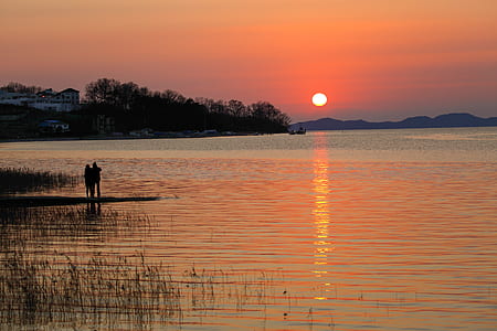 silhouette of two persons standing by the lake at golden hour thumbnail