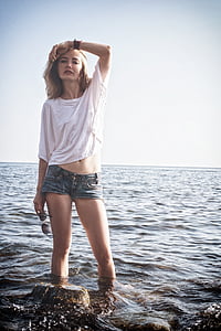 woman wearing white shirt and blue denim short shorts standing near rock on seashore at daytime thumbnail