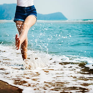 woman barefoot on beach kicking waters at daytime thumbnail