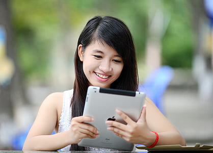 woman with white floral sleeveless shirt using silver iPad close-up photography thumbnail
