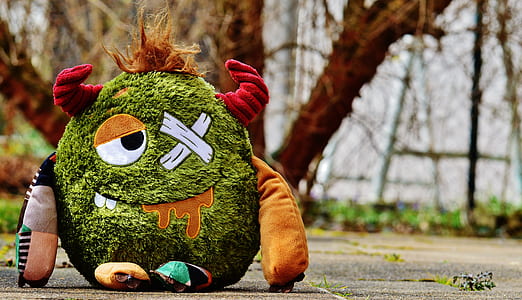 green, orange, and red monster plush toy on gray pavement thumbnail