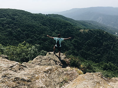man standing on rock facing on green mountain during daytime thumbnail