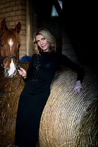 woman leaning against bale of hay while holding horse thumbnail