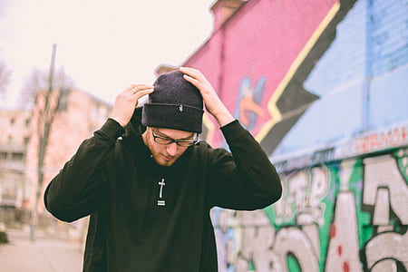 man in black pullover hooded jacket wearing knit cap standing beside wall during daytime thumbnail