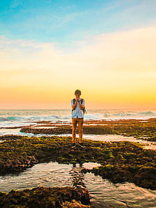 Man Standing on Rocks Near Beach during Golden Hour thumbnail