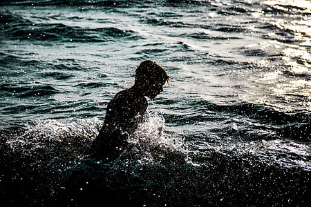 silhouette of person swims in body of water during daytime thumbnail