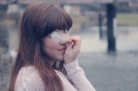 woman in white long-sleeved top holding feather thumbnail