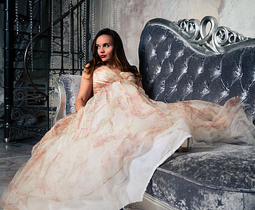 woman wearing white and red strapless dress sitting on black velvet tufted sofa thumbnail