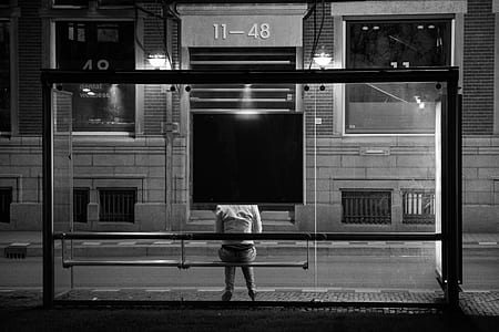 person sitting on bench beside glass building during nighttime thumbnail