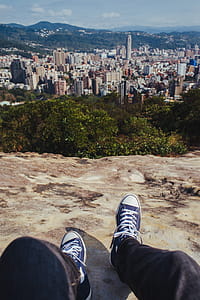 Person Sitting on Brown Rock Cliff While Overlooking on City Buildings thumbnail