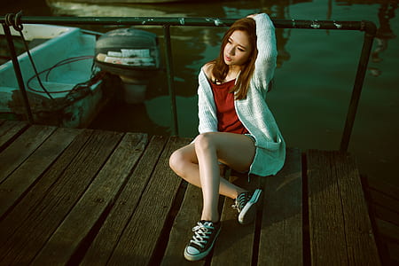 woman wearing red shirt, gray cardigan, and pair of black low-top sneakers outfit sitting on brown wooden dock thumbnail