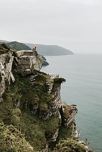 man sitting on cliff above body of water thumbnail