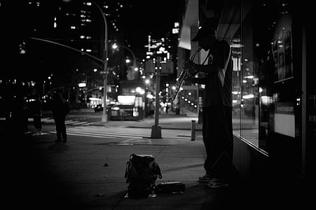 grayscale photography of man playing wind instrument beside a building thumbnail