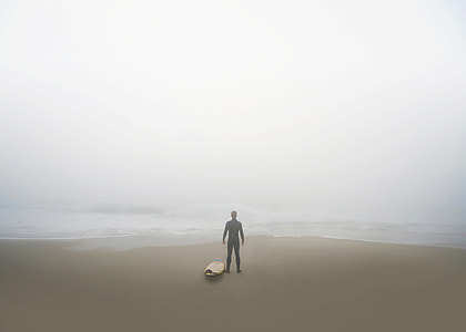 silhouette of person standing facing body of water near surfboard thumbnail