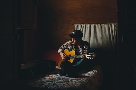 man playing classical guitar sitting on bed comforter thumbnail