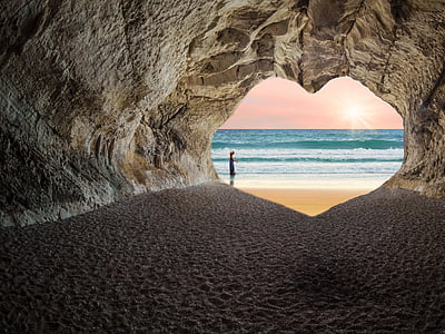 person standing outside heart-shaped cave entrance near sea thumbnail