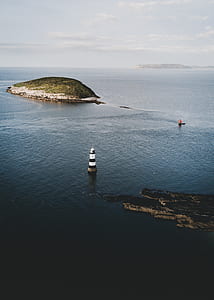 aerial photography of lighthouse near green island at daytime thumbnail