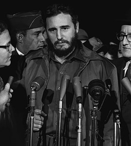 gray scale photo of man wearing black button-up coat in front of five microphones thumbnail