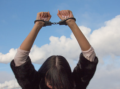 woman wearing black and white shirt raising hands with gray handcuffs during daytime thumbnail