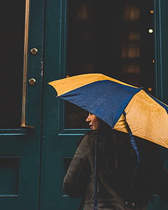 woman holding yellow and blue umbrella in front of door thumbnail