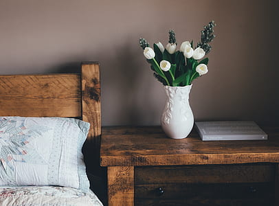 white tulips on white ceramic vase on nightstand beside bed thumbnail