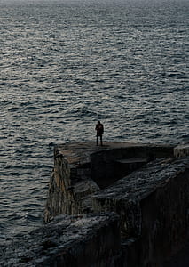 man standing on cliff near body of water thumbnail