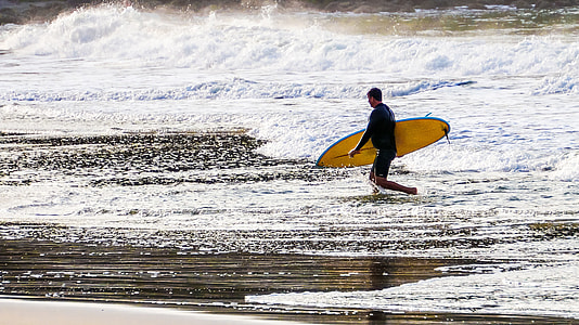 person holding yellow surfboard while walking on seashore thumbnail