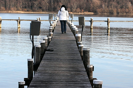 woman walking on wooden bridge on lake during daytime thumbnail