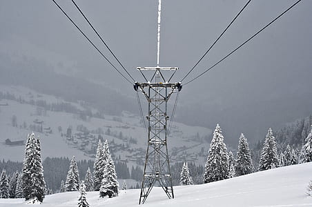 grey transmission tower on snow mountains surrounded by pine trees thumbnail
