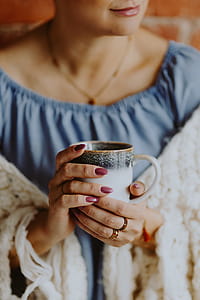 A woman in a warm blanket holds a cup of coffee or tea thumbnail