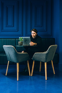 man using MacBook while sitting on green sofa inside room thumbnail