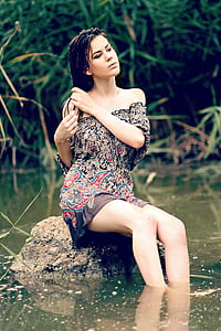 women's wearing gray paisley strapless dress sitting on gray concrete rock with body of water thumbnail