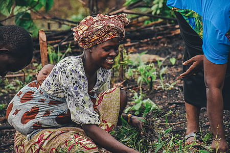 woman holding grass carrying baby at her back beside person bending over thumbnail