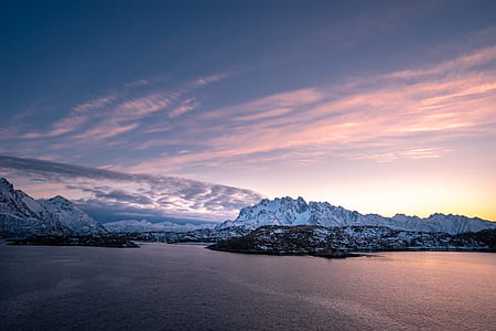 photo of white mountains near body of water under cloudy sky thumbnail