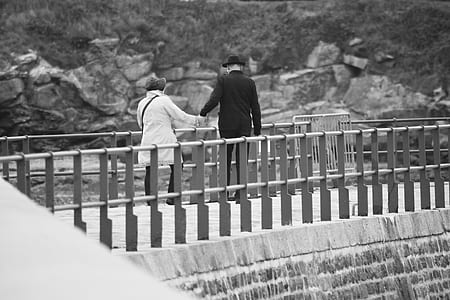 grayscale photo of man and woman holding hands walking at the bridge thumbnail