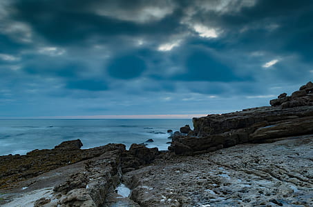 sea near cliff under gray and white cloudy sky thumbnail