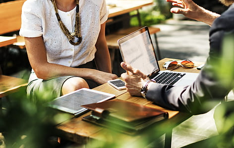 man in black suit holding laptop sitting in front of woman wearing white blouse thumbnail