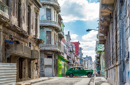 green car between two brown concrete buildings during daytime thumbnail