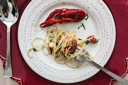 Fancy dinner with seafood pasta, crayfish and red wine by the table decorated with roses thumbnail
