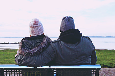 two people sitting on outdoor bench looking at body of water during daytime thumbnail